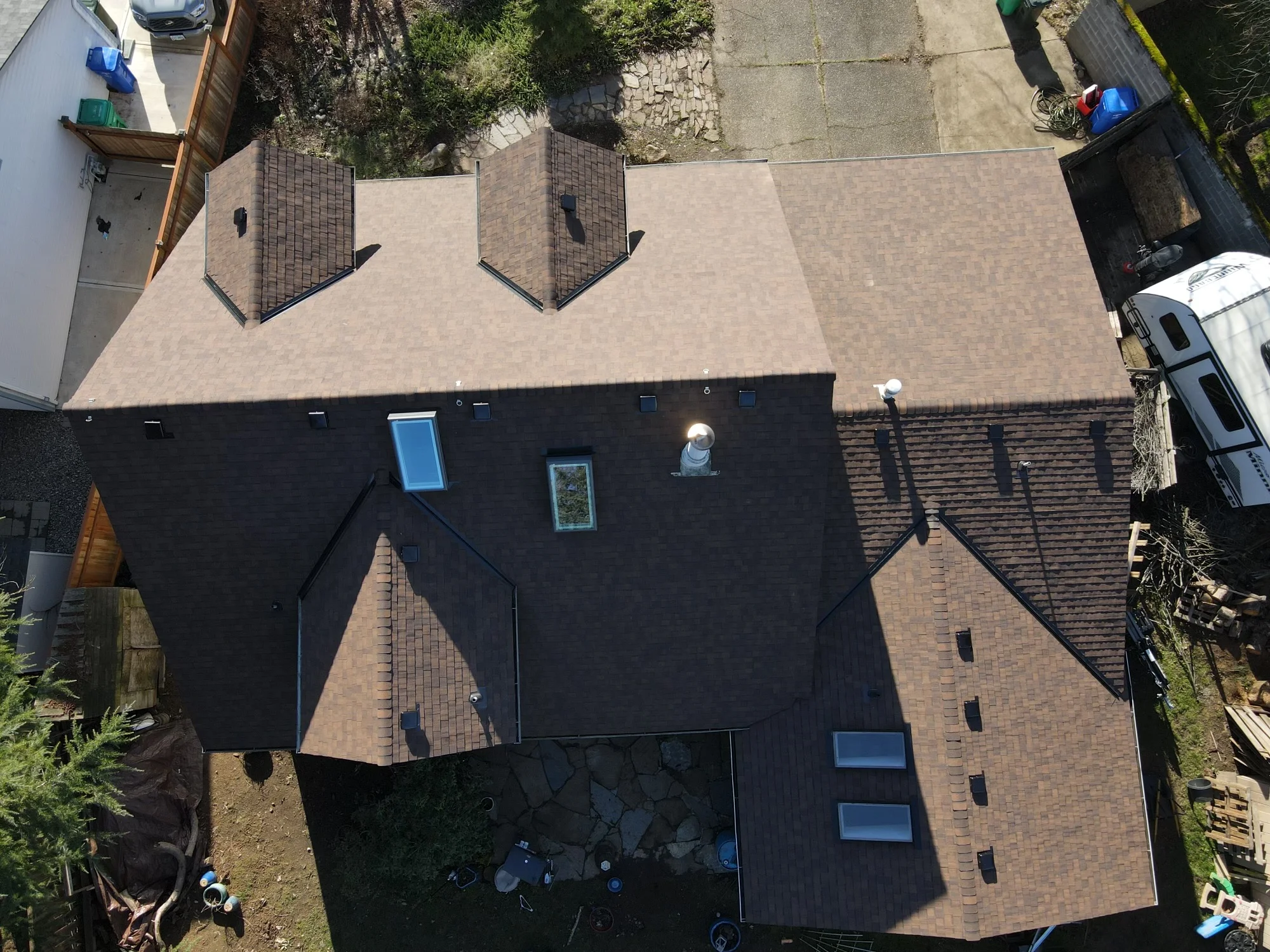 Aerial view of residential roof with brown architectural shingles, multiple slopes, and installed skylights