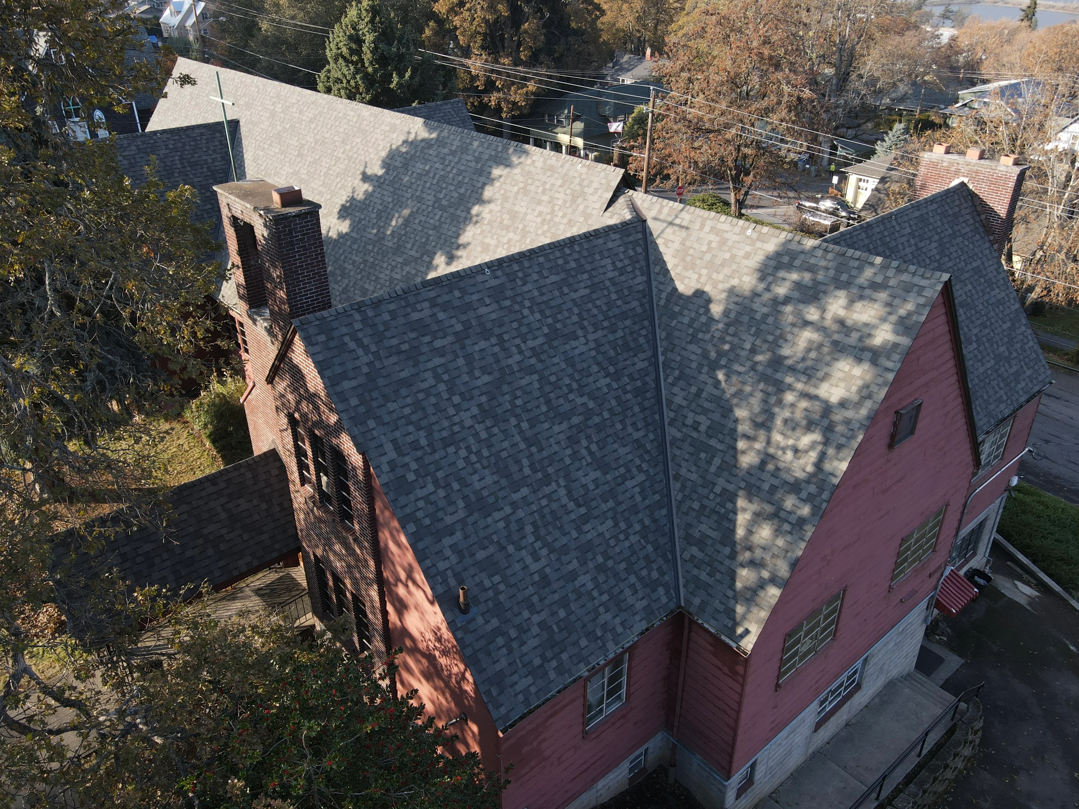 Aerial view of completed asphalt shingle roof installation on two-story home with brick chimney