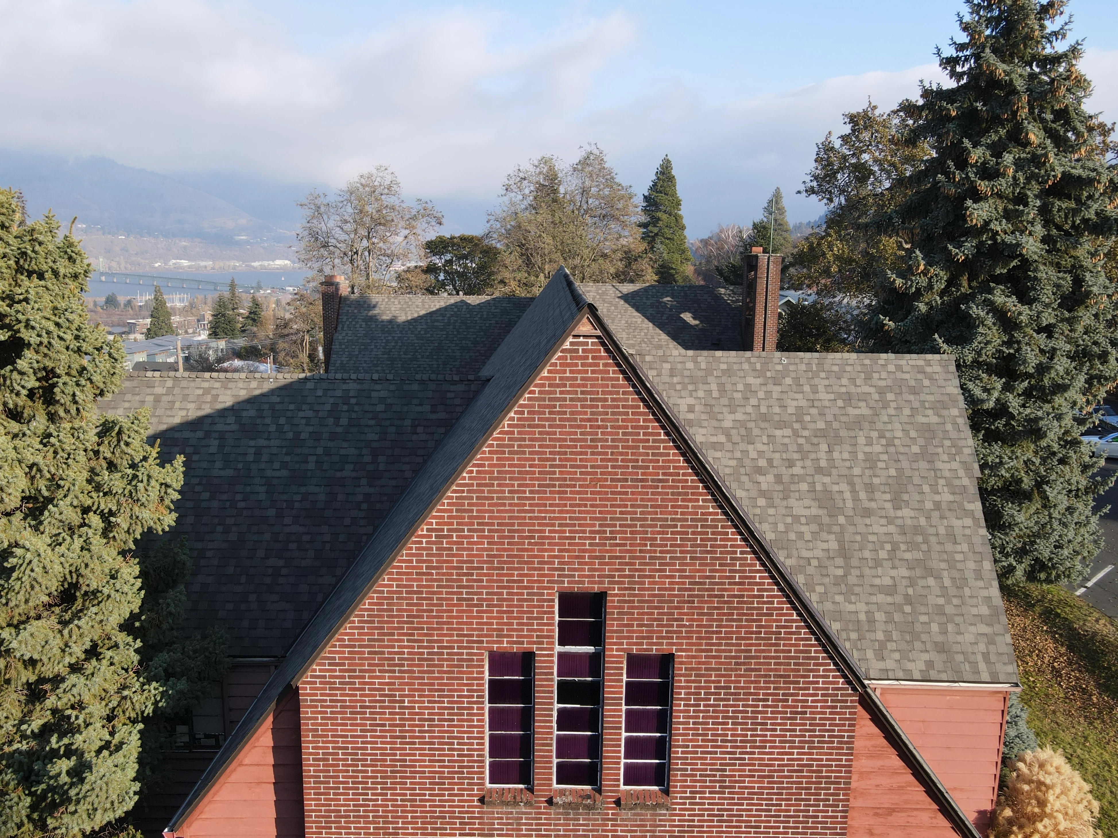 Charcoal gray architectural shingle roof on brick home with two chimneys and multiple roof planes